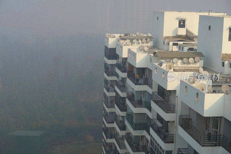 这是印度北方邦新德里的印度公寓楼屋顶的图片，显示了早晨雾蒙蒙的天空污染，被污染的雾，德里的污染照片汽车尾气/工厂排放